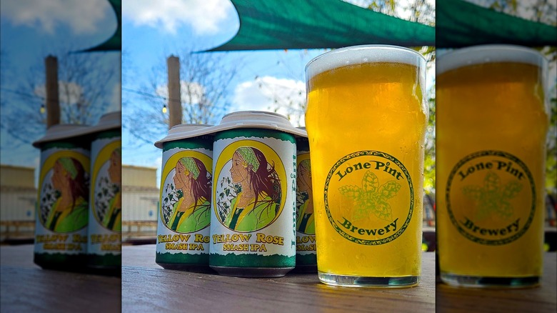 A pack of Yellow Rose cans outside on a picnic table next to a Lone Pint Brewery pint glass full of a hazy beer