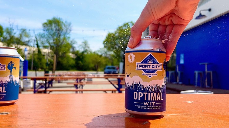A can of Port City Optimal Wit being opened on an outdoor picnic table