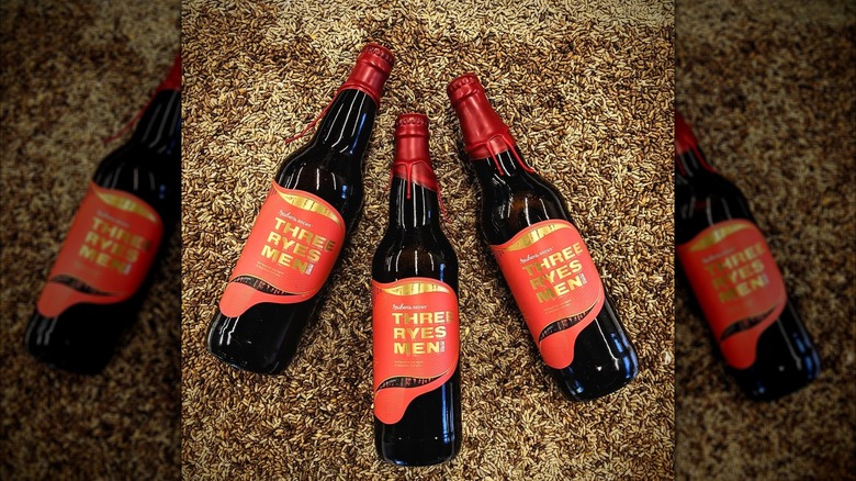Three wax-sealed bottles of Reuben's Brews Three Ryes Men on a bed of malted grain