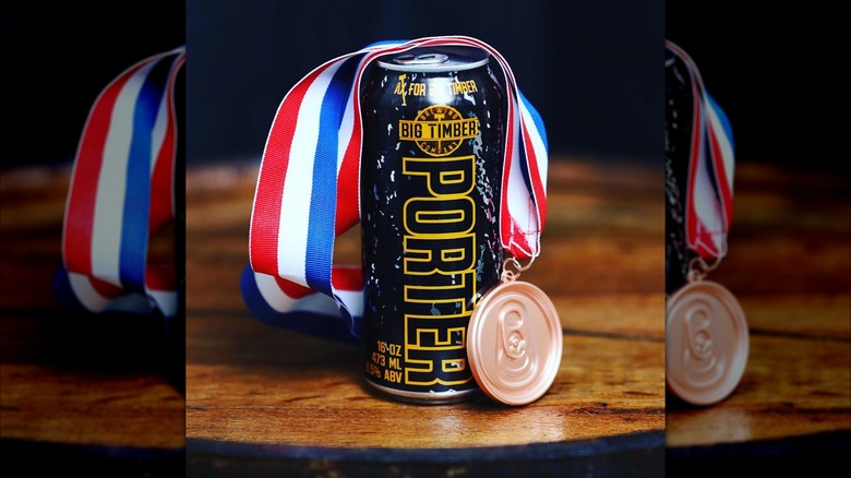 A can of Big Timber Porter draped with a red, white, and blue medal on a wooden surface