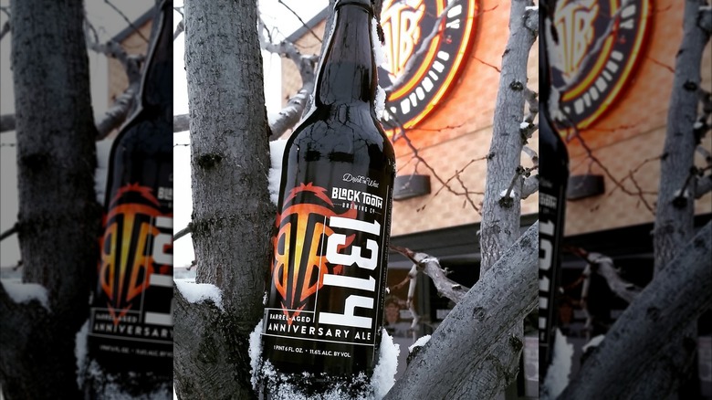 A bottle of Black Tooth Brewing's 1314 wedged between snow-covered tree branches