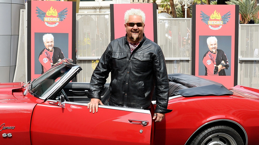 Diners, Drive-Ins and Dives host Guy Fieri smiles in front of red Camaro
