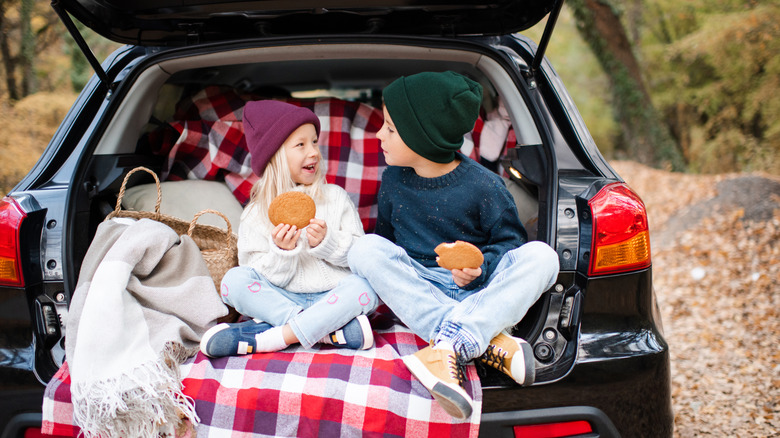 two kids eating snacks in the open trunk of their car