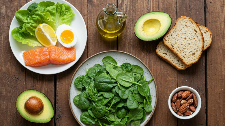 Wooden table filled with fresh, healthy ingredients including salmon, spinach, bread, avocado, and nuts