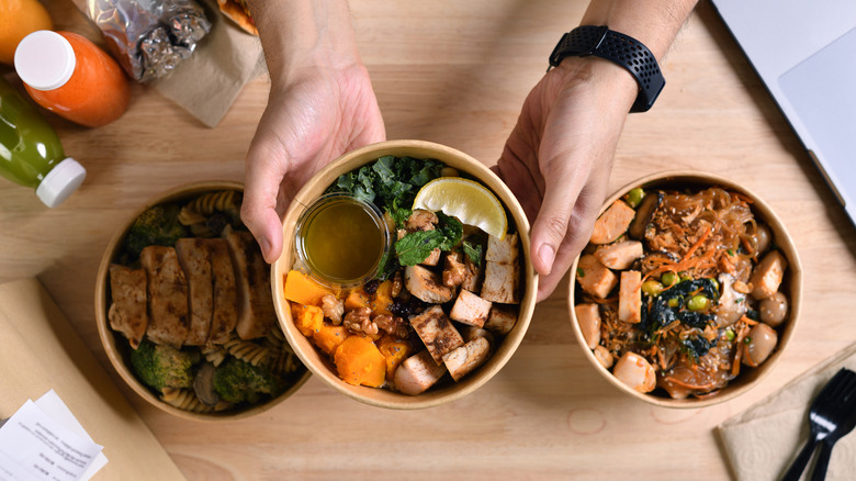 Hands holding a grain bowl with chicken, sweet potato, and kale