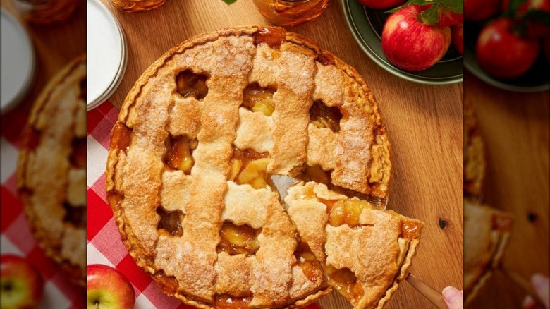 Lattice apple pie sliced on table with apples