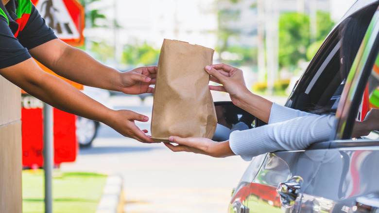 Fast food worker handing bag of food to customer in car