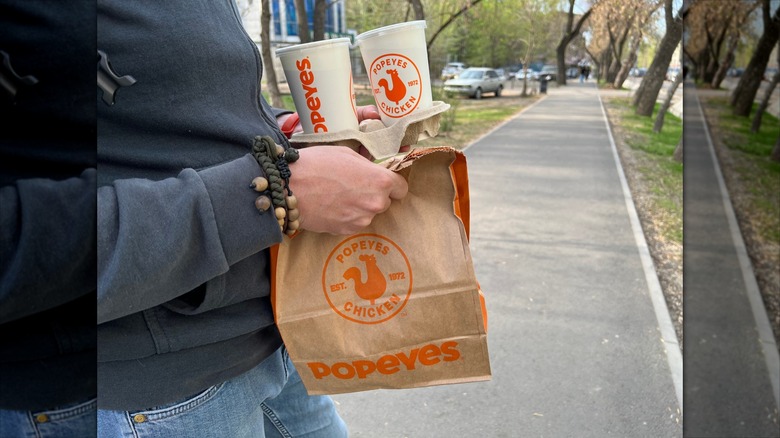 Person holding paper bag and drinks from Popeyes