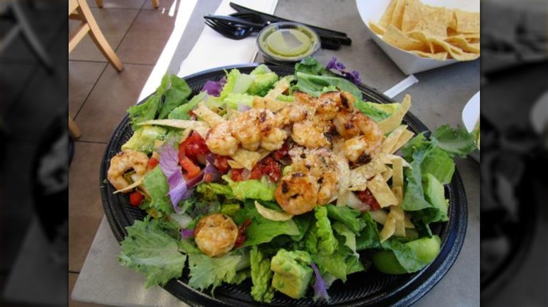 Grilled shrimp on takeout salad at Baja Fresh with sauce and side of tortilla chips on side