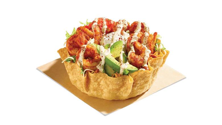 Tostada shell with shrimp, avocado, seasoned rice, and drizzled sauce