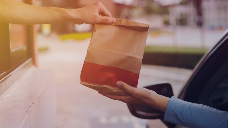 Employee hands paper bag through drive-thru window to customer in car