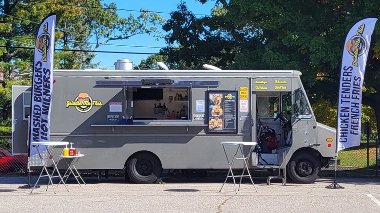 Griddle Me This gray food truck parked with two tables and signs