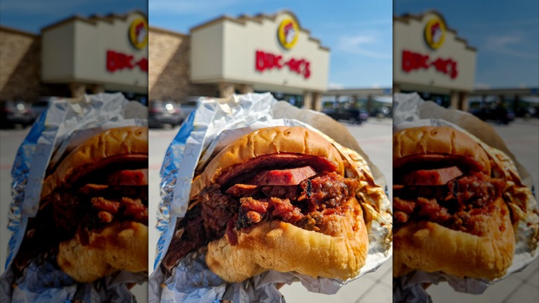 Three-meat barbecue sandwich half-unwrapped with a Buc-ee's gas station in the background