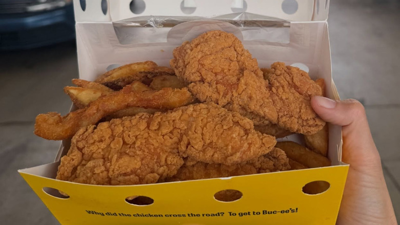 hand holding an open Chicken & Fries box outside a Buc-ee's