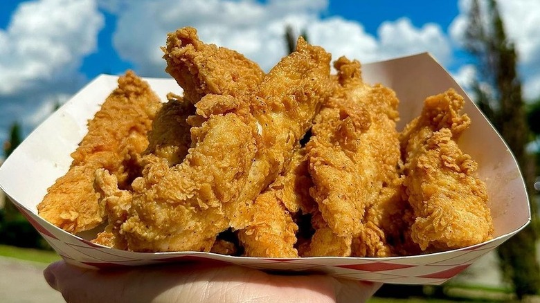 hand holding a tray of Krispy Krunchy Chicken tenders outdoors
