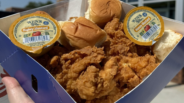 hand holding a box full of Spinx chicken, rolls, and Ken's Honey Mustard sauce