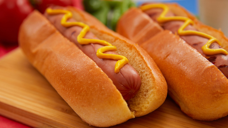 Two grilled hot dogs with mustard on wooden cutting board