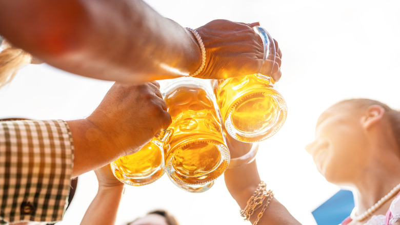 Four friends clinking glass steins of beer outdoors.