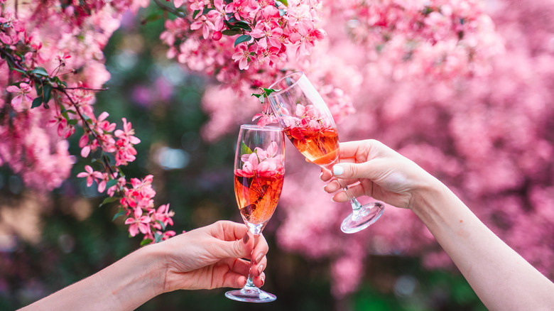 Two hands holding cocktails in front of cherry blossoms