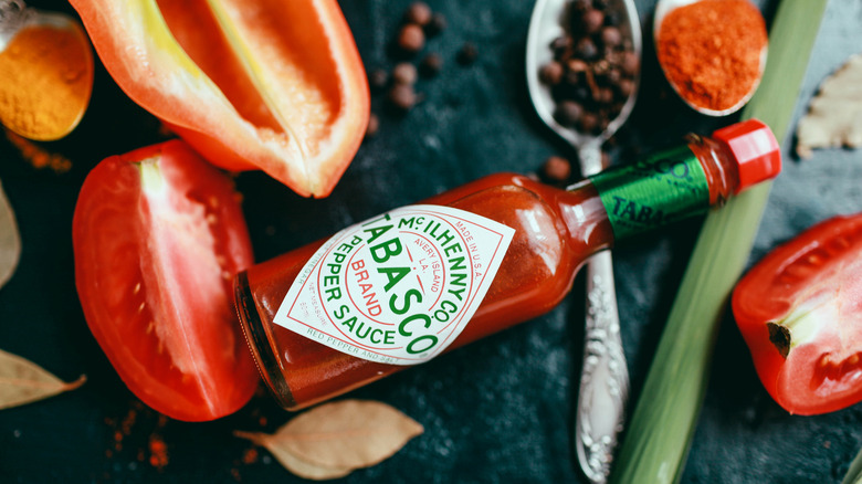 A bottle of Tabasco surrounded by vegetables and spices