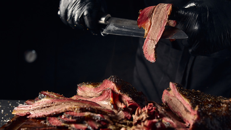 Person slicing brisket with large knife