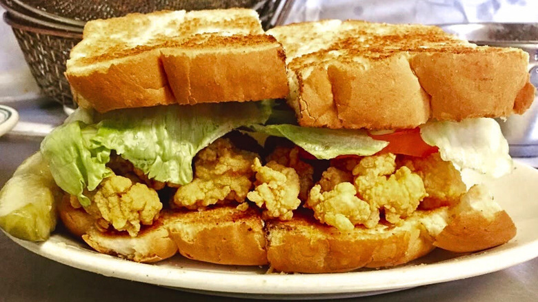 Casamento's oyster loaf sandwich with fried oysters, lettuce, and tomato on toast, served with pickle spear on the side