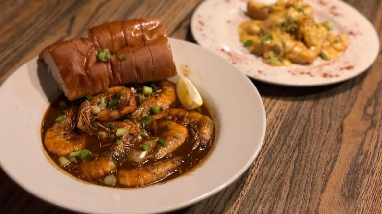 Bowl of Coop's Place New Orleans style BBQ shrimp served with French bread and a side of shrimp and grits