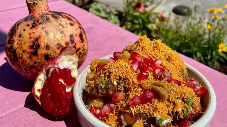 Bowl of Plume Algiers banana chaat topped with pomegranate seeds and crispy sev, photographed beside fresh pomegranates