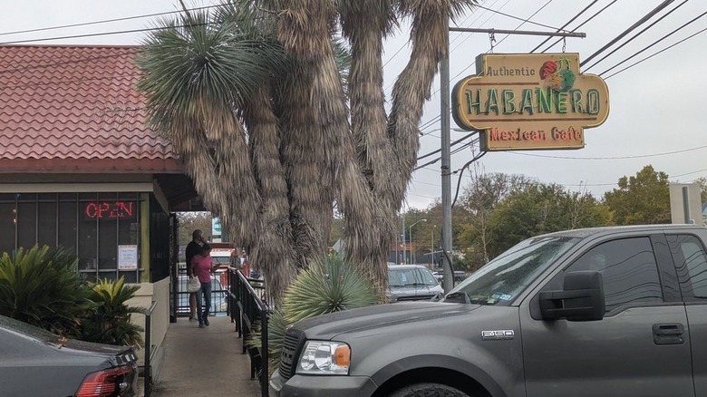 Two people leaving a small cafe with a red roof and a neon sign out front