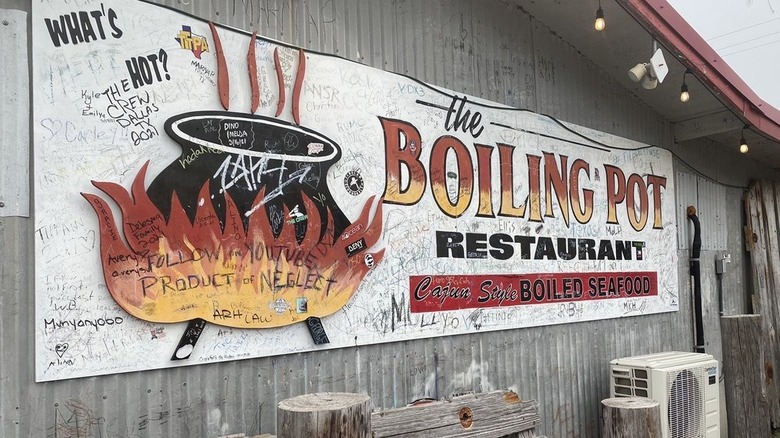 A hand-painted sign of a black kettle boiling on an open fie on the side of a weathered wooden building.