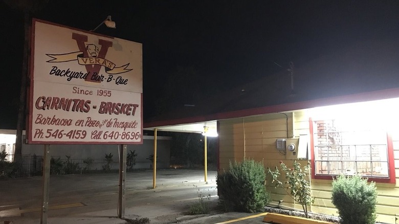 A yellow, wooden restaurant at night with a sign advertising Vera's BBQ