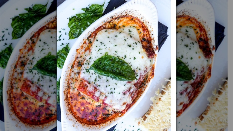 Lasagna in oval dish, garnished with a basil leaf
