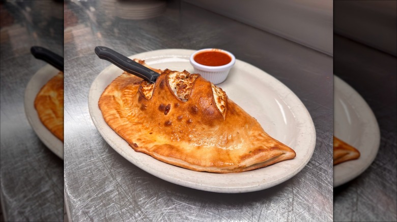Calzone on a plate with a knife in it, accompanied by marinara