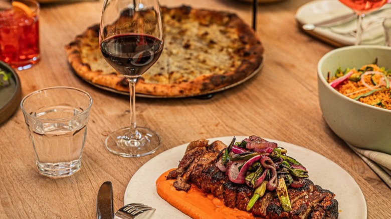A table with pizza and a plate of meat with carrot sauce, along with glasses of wine, aperol, and water