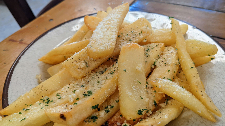 Steak fries with herbs and Romano cheese on white plate.