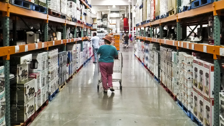 A shopper checks out products as they push a cart down an aisle in Costco.