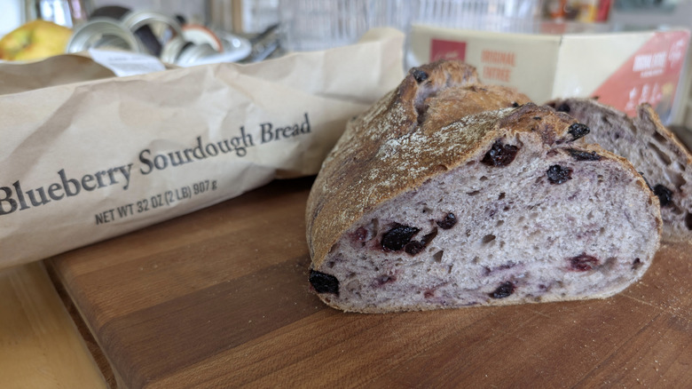 A loaf of Kirkland Blueberry Sourdough Bread cut in half on cutting board with bag in background.