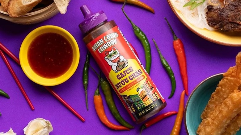 Bottle of Asian Cajun Cowboy Nước Châm sauce surrounded by chili peppers and dishes of food
