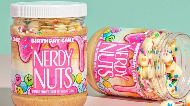 Two jars of Nerdy Nuts Birthday Cake Peanut Butter with one open on its side