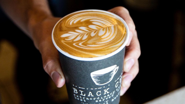 Man holds a coffee drink, showing off its latte art