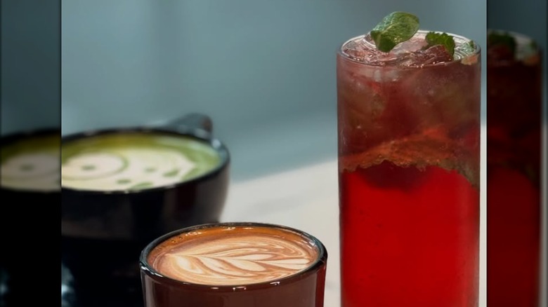 A fruity red iced beverage next to two coffee drinks with latte art