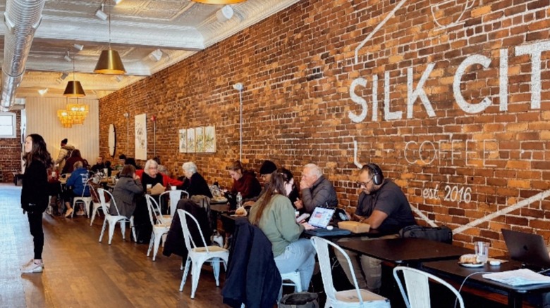 Coffee drinkers seated at row of tables along a brick wall with text that reads Silk City Coffee