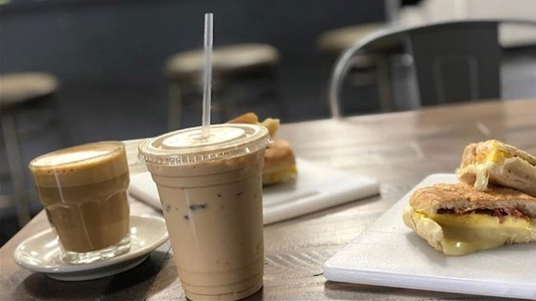 An iced coffee, a coffee in a short glass, and some breakfast sandwiches on a table
