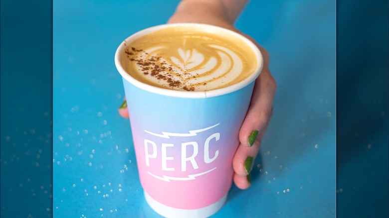A person holds a pink and blue Perc cup of coffee, showing off its latte art