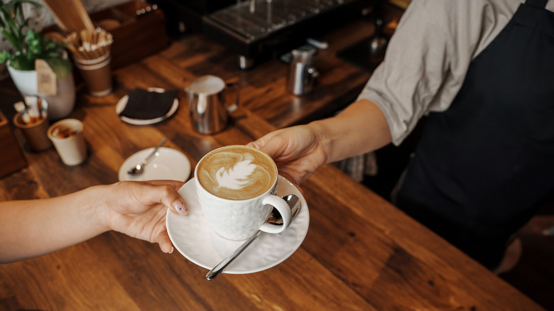 Barista hands a latte to a customer over a counter