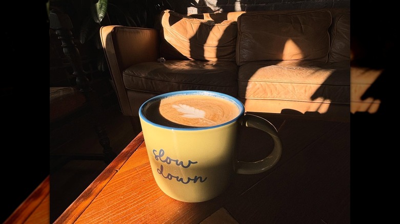 A latte in a yellow coffee mug with slow down printed on it
