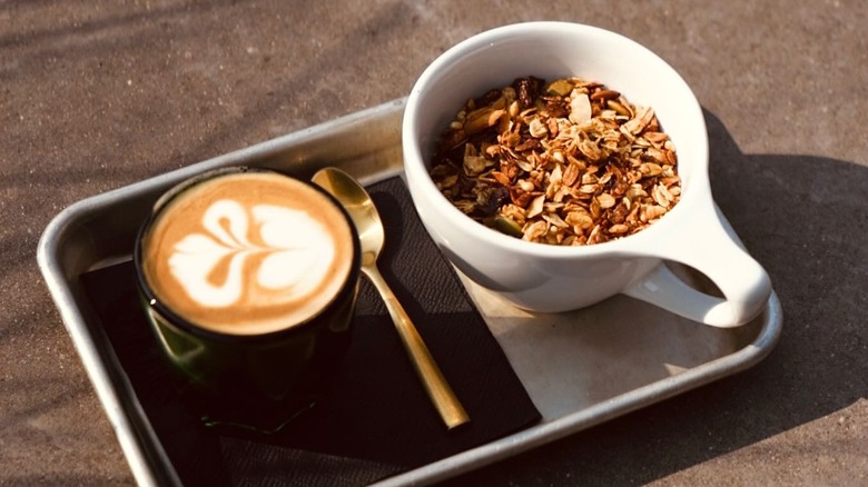 Latte with foam art next to a bowl of oats on a try
