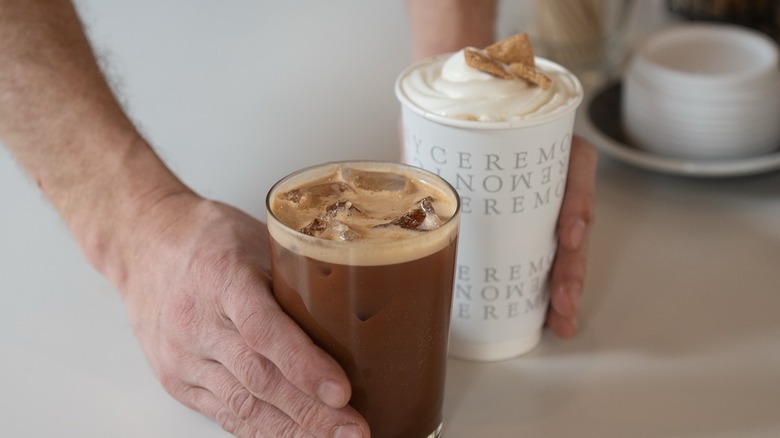 Man holds a whipped cream coffee and iced coffee from Ceremony Coffee Roasters