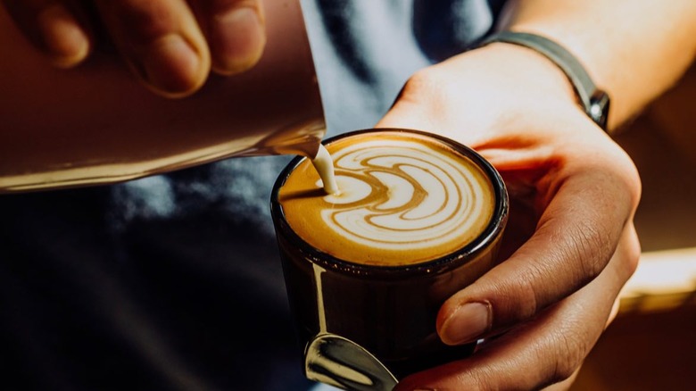 Barista pours milk into a cup of coffee to create latte art