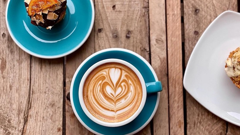 Coffee with latte art sits next to various pastries on a wooden table